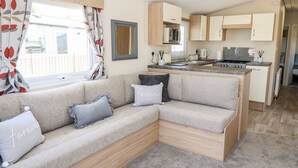 A cozy RV interior with a sofa, a kitchen area, and a window with curtains. - 3 Bed New Lodge, Sleeps 4, Pets Welcome (Scunthorpe)