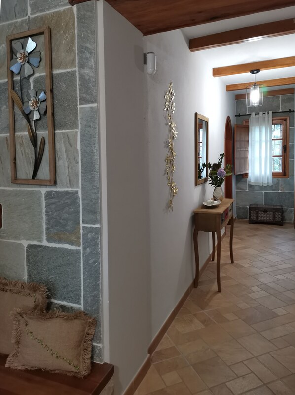 A hallway with stone walls, a wooden bench, a decorative metal piece, a mirror, and a window with a curtain.