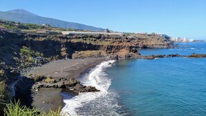 A coastal landscape with a rocky beach, clear blue sea, and a distant mountain. - Finca Vista al Teide with private swimmingpool and jacuzzi, Wifi and Sat TV (Santa Úrsula)