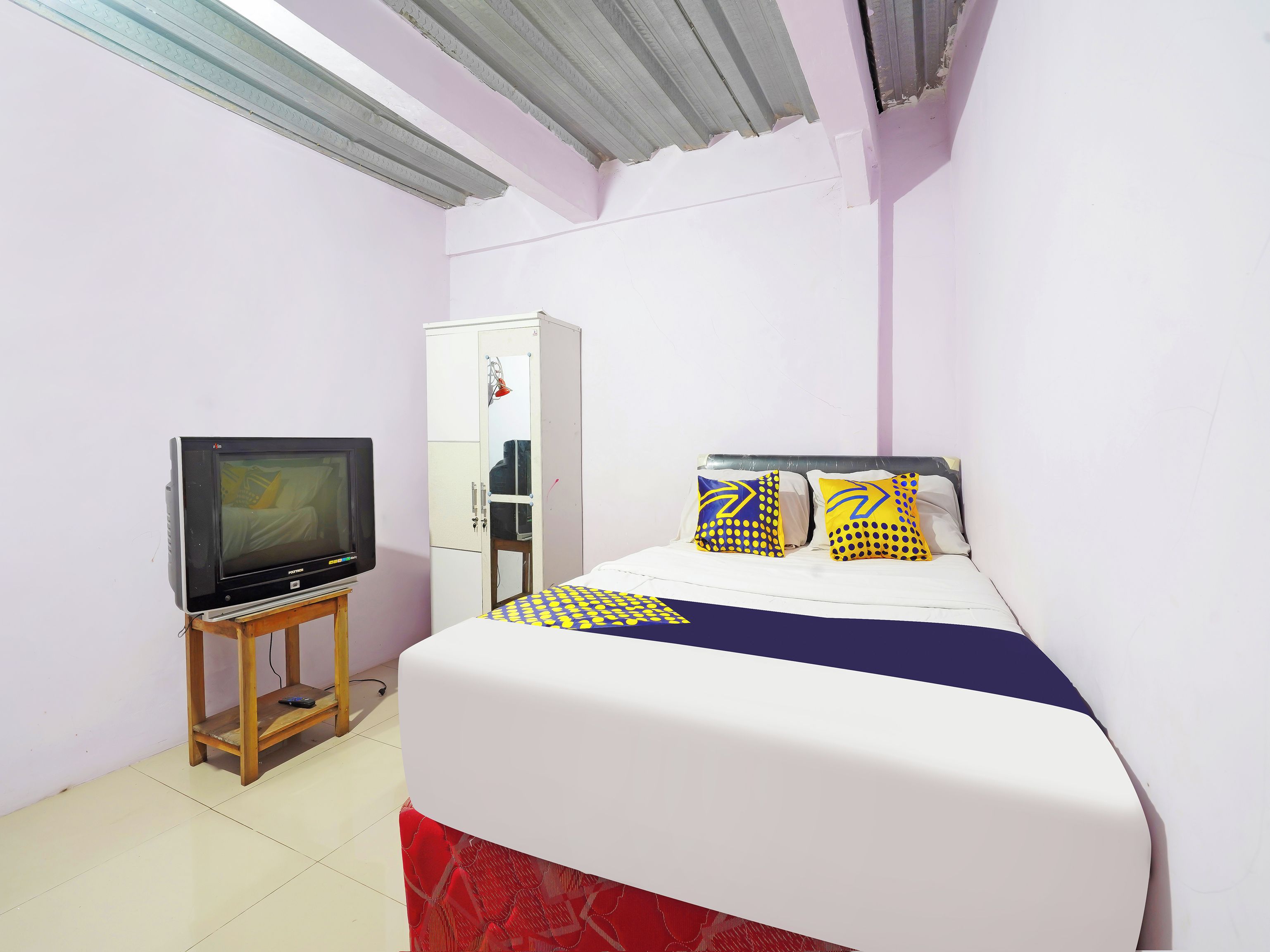A small, single-bed room with a television on a wooden stand, a wardrobe, and a bed with patterned bedding.