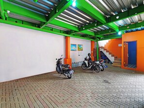 A covered parking area with two scooters parked, a staircase, and a door to a room. - Hotel O Biring Residence (Wargasaluyu)