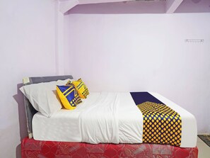Cama com roupa de cama branca, duas almofadas com estampas azuis e amarelas, e saia de cama vermelha estampada.