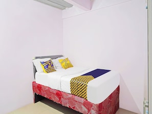 Een bed met witte lakens, twee kussens met gele en blauwe patronen, en een rood bedsprei.