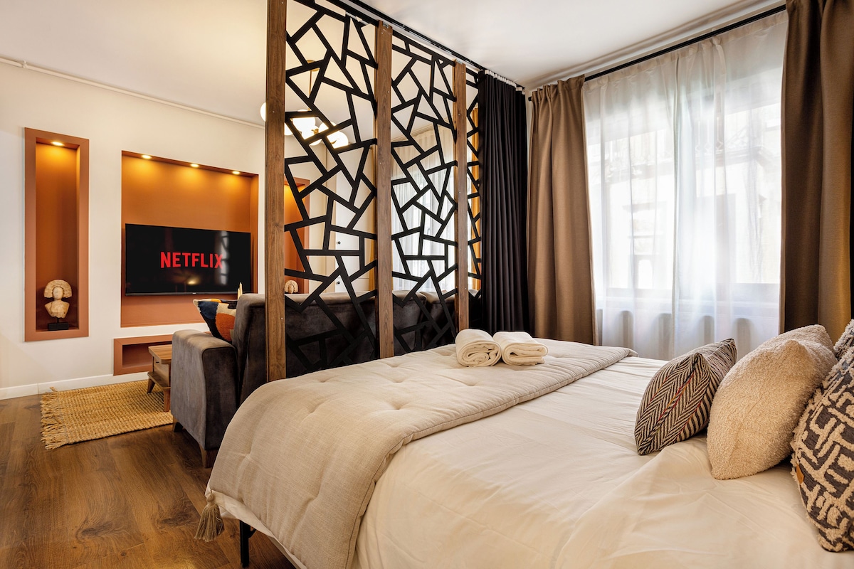 A modern hotel room with a large bed, a desk with a TV, and a decorative wall panel.