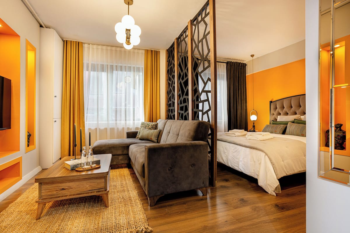 A modern hotel room with a sofa, a bed, a wooden coffee table, and a decorative partition.