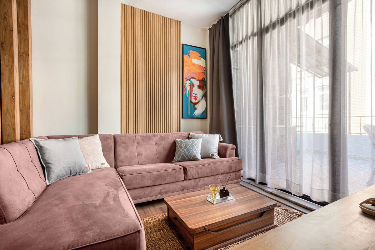 A modern living room with a sectional sofa, a wooden coffee table, and a large window with sheer curtains.