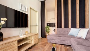 Een moderne woonkamer met een flatscreen televisie, een houten entertainmentkast en een grijze bank met kussens.