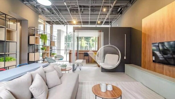 Un soggiorno moderno con un divano, una poltrona sospesa, un tavolino da caffè e una TV a parete.