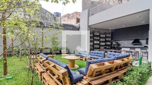 Un'area esterna moderna con sedute in pallet di legno e cuscini blu, un piccolo tavolino rotondo e un angolo cottura con cappa nera e piano di lavoro rivestito di piastrelle.