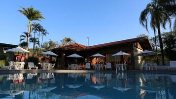 A pool area with lounge chairs and umbrellas, surrounded by palm trees and a building with a red roof.