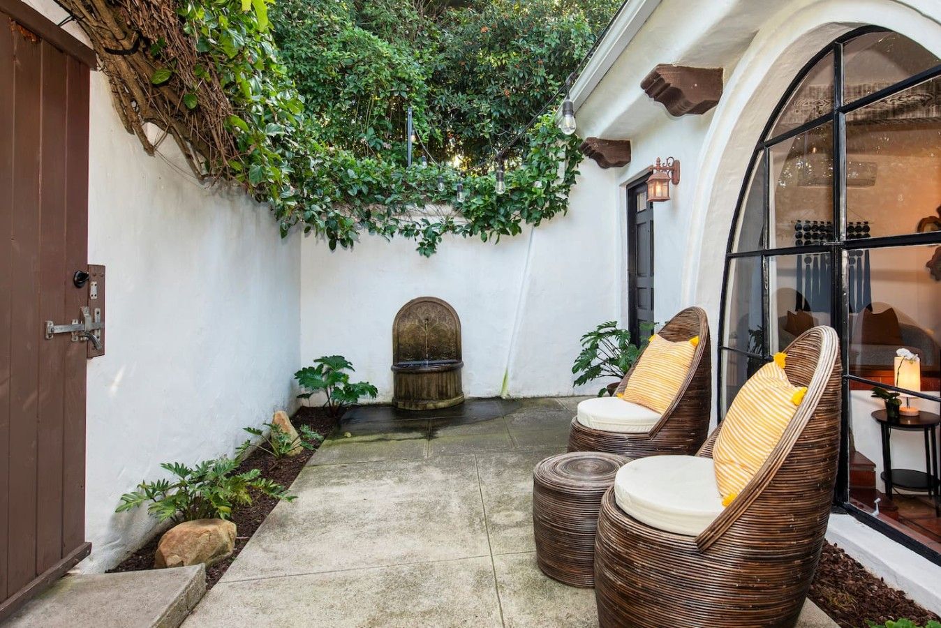 A courtyard with a fountain, two wicker chairs, and a door.