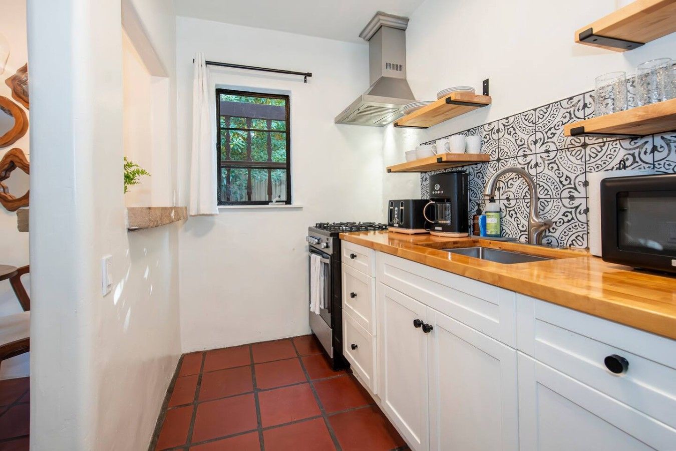 A compact kitchen with white cabinets, a wooden countertop, a gas stove, a microwave, and a patterned backsplash.