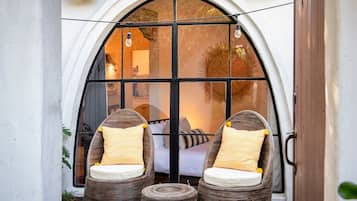 A room with a large arched window, two wicker chairs with cushions, and a small round table.