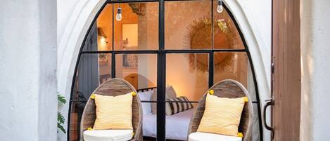 A room with a large arched window, two wicker chairs with cushions, and a small round table.