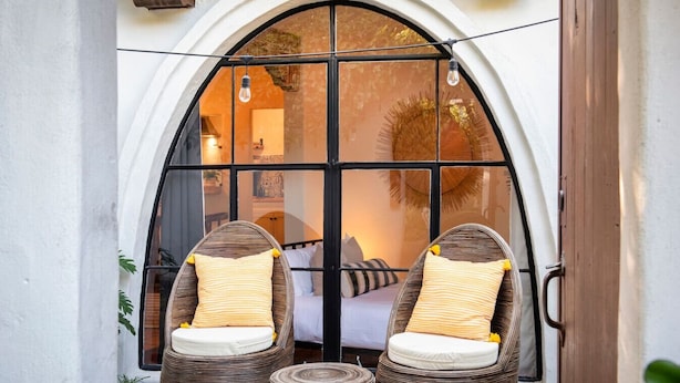 A room with a large arched window, two wicker chairs with cushions, and a small round table. - Charming Studio Hideaway in Montecito (Montecito)