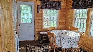 L’intérieur d’un chalet en bois comprend une table à manger, des chaises, un tapis à motifs et une porte ornée d’un vitrail.