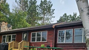 Une cabane en rondins avec une terrasse en bois, une table de pique-nique et un mur en pierre.