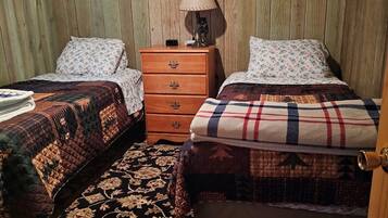 A cozy bedroom with two beds, a wooden dresser, a patterned rug, and a wall clock.