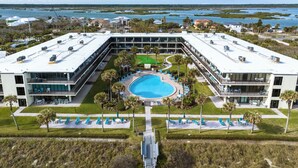 A modern hotel with a central pool, multiple balconies, and a view of the surrounding water and greenery. - Ocean House 311 by Distinctive Beach Rentals (St. Augustine)