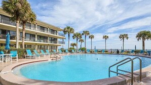 A swimming pool with lounge chairs and palm trees, surrounded by a building with balconies. - Ocean House 311 by Distinctive Beach Rentals (St. Augustine)