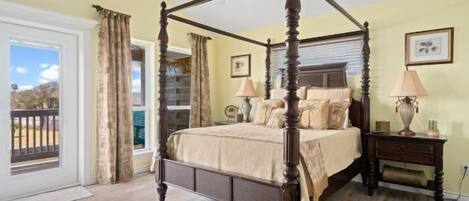 Un lit à baldaquin dans une chambre avec balcon, une table de chevet avec des lampes et un tableau encadré au mur.
