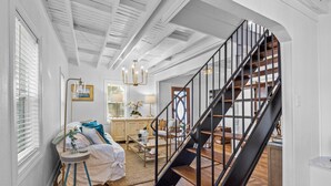 Eine Treppe mit schwarzer Geländer, die zu einer zweiten Etage führt, ein runder Couchtisch mit Glasplatte und ein weißes Sofa mit blauer Decke.