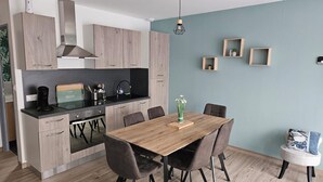 Una cocina moderna con armarios de madera, encimera negra y zona de comedor con mesa y sillas de madera.
