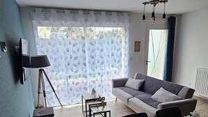 Una sala de estar moderna con sofá, mesa de comedor y sillas. Hay una lámpara de trípode y una mesita con objetos decorativos.