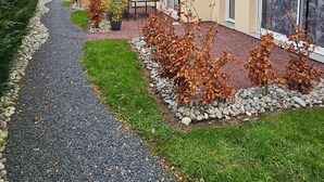 Propiedad residencial con camino de grava, cerca de madera y jardín con arbustos y una mesa.