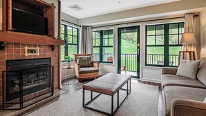 A living room with a fireplace, a sofa, a coffee table, and a television on a wooden shelf. - Heated Pool Hot Tubs Sauna Gym Deck Mtn Front Appalachian @ Mtn Creek #246/248 (Vernon)