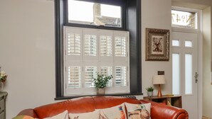 A room with a brown leather sofa, a window with shutters, a framed picture, and a small table with a lamp. - No 47, Haworth (Keighley)