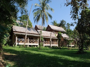 A bungalow with a thatched roof, wooden balconies, and surrounded by lush greenery. - My Dream Boutique Resort (Luang Prabang)