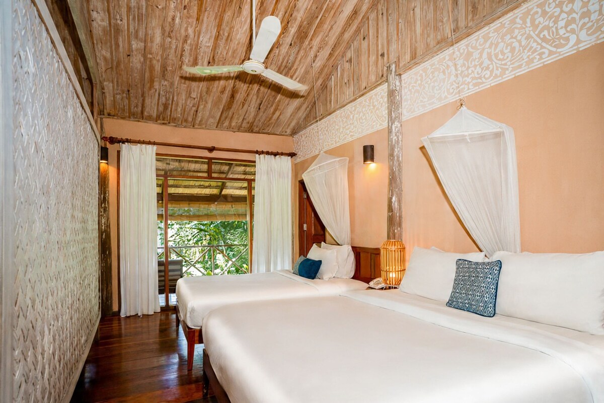 A bedroom with a wooden ceiling, a bed with white bedding, a bedside table with a lamp, and a window with curtains.