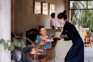 A person seated in a wicker chair, another person standing beside them, and a table with a tray. - My Dream Boutique Resort (Luang Prabang)