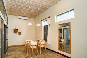 Un coin repas avec une table et des chaises en bois, un grand miroir et une fenêtre avec des rideaux.