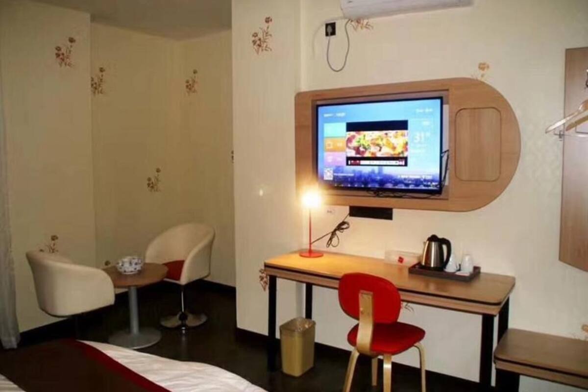 Una habitación de hotel con cama, escritorio con silla, televisor y una mesita con tetera.