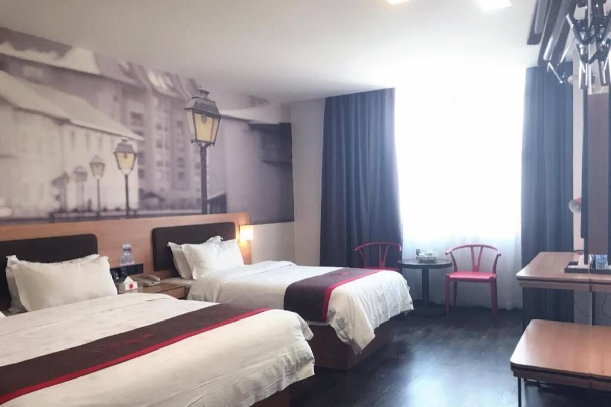 Habitación de hotel con dos camas, una mesita, una silla y un mural en la pared.