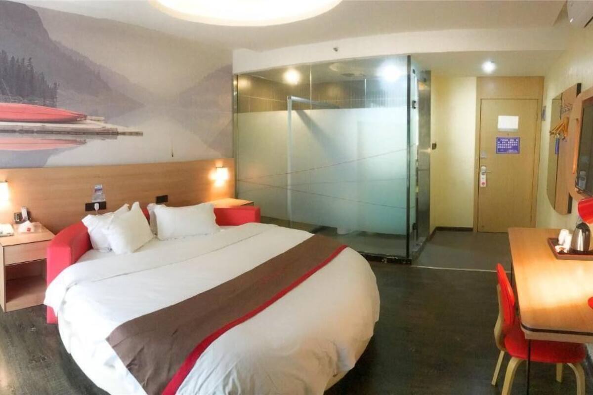 Habitación de hotel con cama, escritorio, silla, espejo, ducha y un cuadro de un paisaje montañoso.