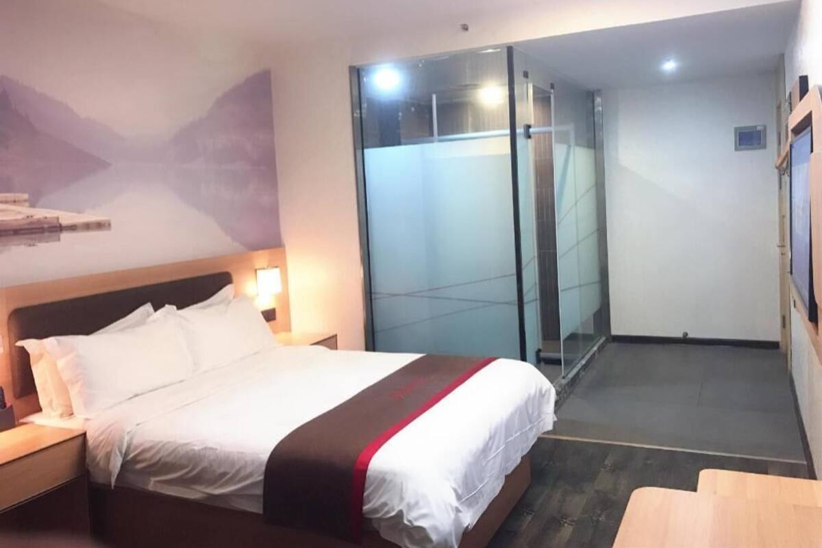 Una habitación de hotel con cama, mesita de noche, cabina de ducha de vidrio y un banco de madera.