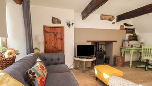 A cozy living room with a grey sofa, a yellow ottoman, a wooden door, a fireplace, and a green chair.
