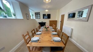 Une salle à manger avec une longue table en bois, dressée pour six personnes, et entourée de chaises en bois dotées de coussins noirs.