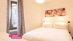 Habitación de hotel ordenada con cama, ventana con cortinas, radiador y aplique de pared.