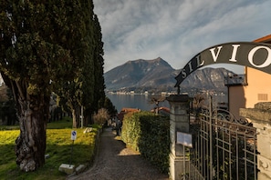 A pathway leading to a gate with the inscription "SILVIO" against a backdrop of mountains and a lake. - Loppia Bay by Wonderful Italy (Bellagio)