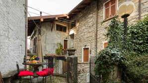 Un patio estrecho con un edificio de piedra, una mesa con sillas y un farol.