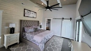 A bedroom with a tufted headboard, a bed with a patterned bedspread, a ceiling fan, and a view of the outdoors. - HOT TUB & Bicycles - Walking distance to the BEACH, bay, restaurants, & shopping (Brigantine)