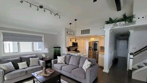 A spacious living room with a grey sofa, a coffee table, and a staircase leading to a kitchen area. - HOT TUB & Bicycles - Walking distance to the BEACH, bay, restaurants, & shopping (Brigantine)