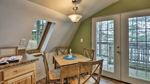 Comedor con mesa y sillas de madera, lámpara en el techo y ventanas amplias con vista a árboles.