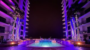 A swimming pool area with a central pool, surrounded by palm trees and illuminated by colorful lights. - Tidal Pull 1029-Gulf View Studio-Sleeps 3 (Panama City Beach)