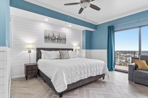 A bedroom with a bed, nightstands, a ceiling fan, a large window with a view, and a balcony.