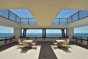 A spacious balcony with a clear view of the ocean, furnished with tables and chairs.